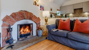 Ein Wohnzimmer mit Kamin, einer Couch, einer Lampe und einer Küche im Hintergrund.