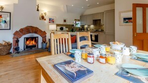 Ein gemütliches Wohnzimmer mit Kamin, ein Essbereich mit einem für das Frühstück gedecktem Tisch und eine Küche im Hintergrund.