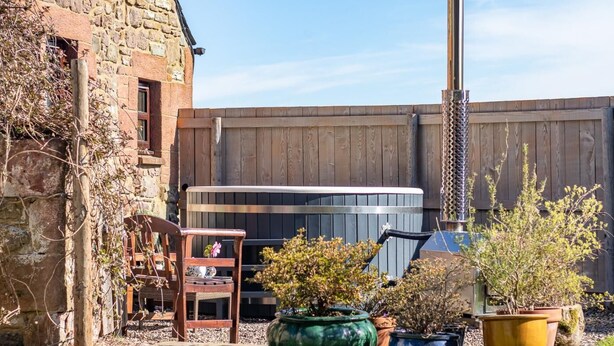Ein Gebäude aus Stein mit einer Holzterrasse, einem Whirlpool und Kübelpflanzen.