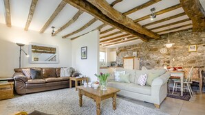A living room with a brown leather sofa, a white sofa, a wooden coffee table, and a stone wall. - 2 Bed in Bude (oc-54244) (Poundstock)