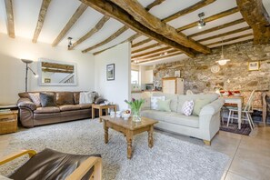 A living room with a brown leather sofa, a white sofa, a wooden coffee table, and a stone wall. - 2 Bed in Bude (oc-54244) (Poundstock)