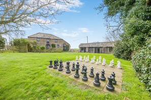 A chessboard set up in a grassy area with stone buildings in the background. - 2 Bed in Bude (oc-54244) (Poundstock)