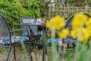 A metal outdoor table with chairs, surrounded by greenery and a wooden fence. - 2 Bed in Bude (oc-54244) (Poundstock)