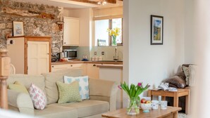 A living room with a sofa, a coffee table, and a kitchen in the background. - 2 Bed in Bude (oc-54244) (Poundstock)