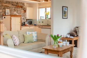 A living room with a sofa, a coffee table, and a kitchen in the background. - 2 Bed in Bude (oc-54244) (Poundstock)