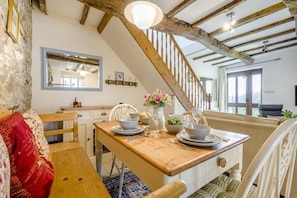 A dining area with a wooden table set for four, a staircase, and a view of the outdoors. - 2 Bed in Bude (oc-54244) (Poundstock)