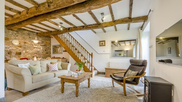 A cozy living room with a stone wall, a wooden staircase, a sofa, a coffee table, and a leather armchair. - 2 Bed in Bude (oc-54244) (Poundstock)