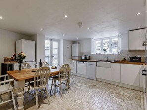 Una cocina con armarios blancos, una mesa de comedor de madera con sillas y una ventana con contraventanas.