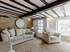 Ein Zimmer mit Steinwand, einer großen Uhr, einem Sofa, einem Sessel und einem Fenster mit Blick.