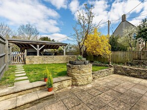 A backyard with a stone patio, a covered barbecue area, and a stone planter with plants. - 3 Bed in Witney (oc-82478) (Hailey)
