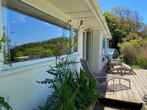 Eine Holzterrasse mit Gartenmöbeln, einem Glasbalkon und Blick ins Grüne.