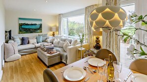 Ein modernes Wohnzimmer mit einer Couch, einem Hocker und einem Esstisch, gedeckt für eine Mahlzeit.