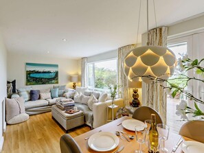 Ein modernes Wohnzimmer mit einer Couch, einem Hocker und einem Esstisch, gedeckt für eine Mahlzeit.