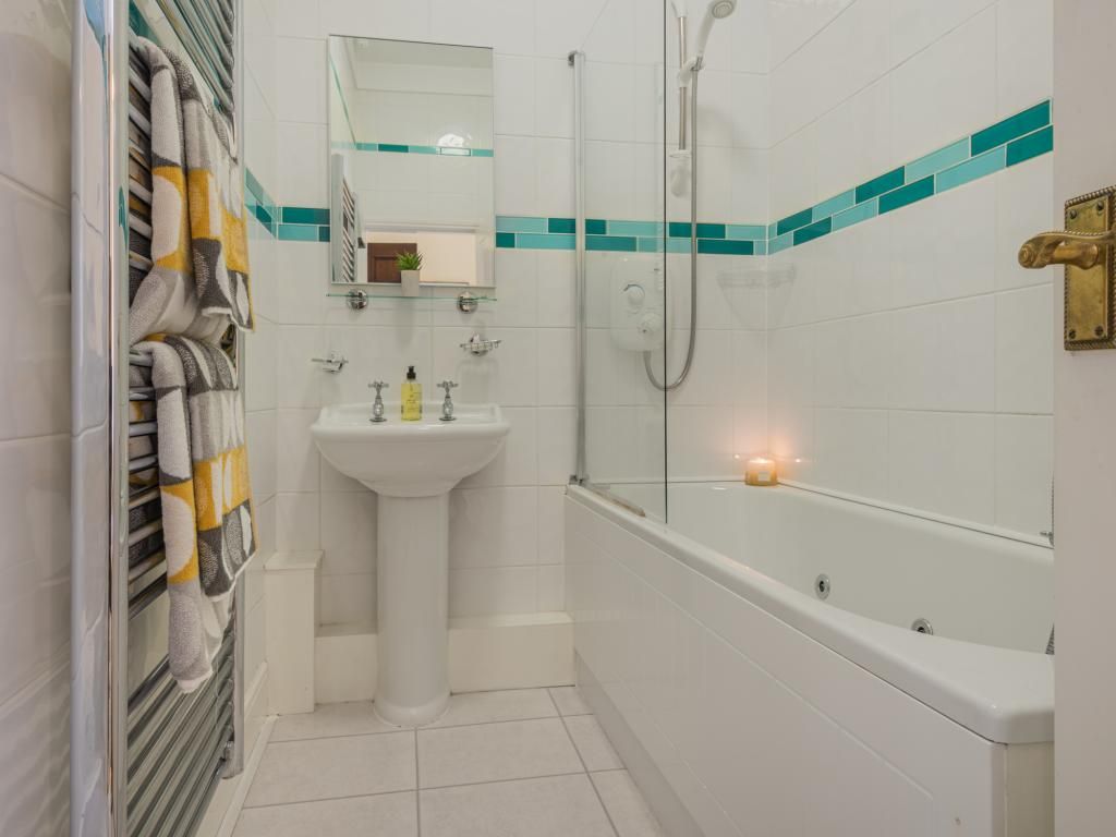 A bathroom with a sink, mirror, towel rack, shower, and a lit candle.