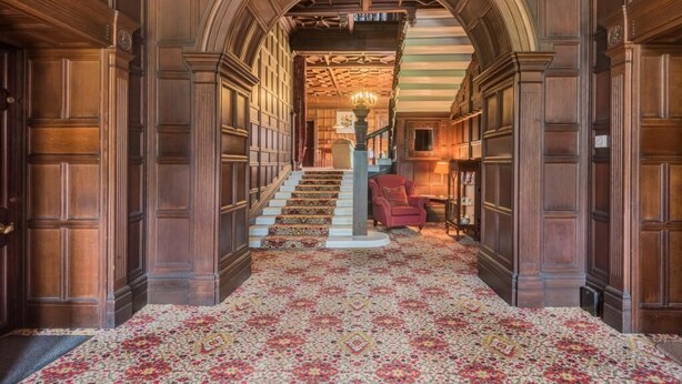 Un vaste hall d’entrée avec un tapis à motifs, des boiseries et un escalier menant à l’étage supérieur.