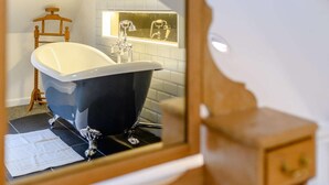 Ein Badezimmer mit einer Badewanne, einem Holzstuhl, einem Spiegel und einer Kachelwand.