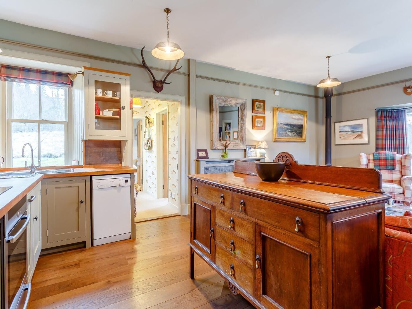 A kitchen with wooden cabinets, a sink, and a dishwasher. There is a hallway leading to another room.