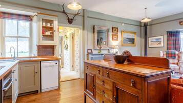 A kitchen with wooden cabinets, a sink, and a dishwasher. There is a hallway leading to another room.