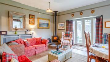 A cozy living room with a sofa, a plaid armchair, a fireplace, and a dining area with a table and chairs.