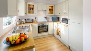 Una cocina moderna con armarios blancos, encimera de madera, un fregadero, un tostador, un hervidor y un bol de fruta.