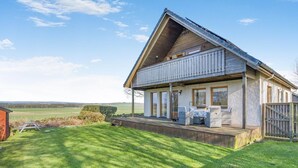 Uma casa de dois andares com varanda, terraço e vista para o campo.