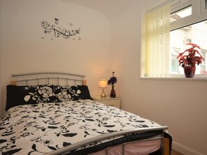 A bedroom with a bed, a nightstand, a lamp, a wall decoration, and a window with a plant. - 1 Bed in Newton Abbot (oc-peboo) (Caton)