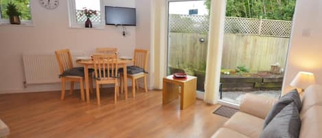 A living room with a wooden dining table, chairs, a sofa, and a TV mounted on the wall.