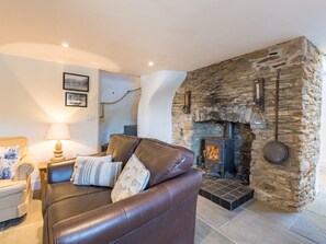 A cozy living room with a stone fireplace, leather sofa, and a lamp. - 5 Bed in Dartmouth (oc-72751) (Dittisham)