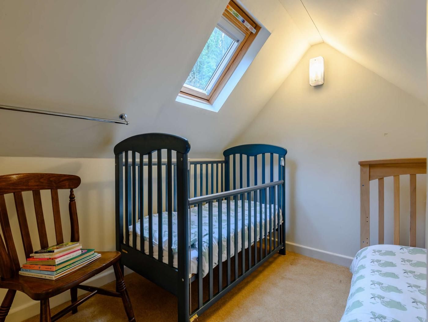 A room with two cribs, a wooden chair, a bookshelf, and a skylight.