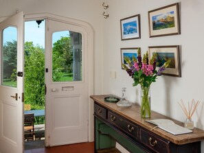 Ein Zimmer mit einer weißen Tür, einem Holztisch mit Blumenvase und gerahmten Bildern an der Wand.