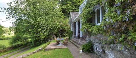A stone building with a garden, a bench, and a plaque on the wall.