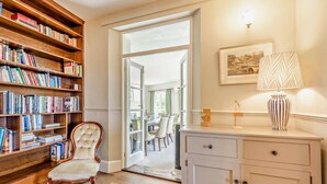 A room with a wooden bookshelf, a white cabinet, a chair, and a dining area in the background. - 6 Bed in Bideford (oc-81507) (Westleigh)