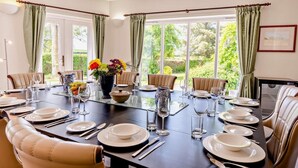A dining room with a long table set for a meal, large windows, and a view of greenery outside. - 6 Bed in Bideford (oc-81507) (Westleigh)
