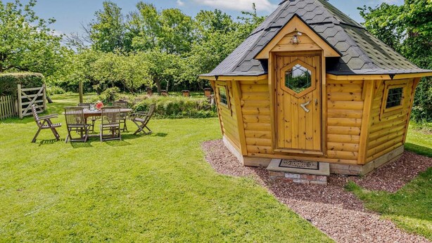 A wooden cabin with a hexagonal door, surrounded by a well-maintained garden and a picnic table with chairs. - 6 Bed in Bideford (oc-81507) (Westleigh)