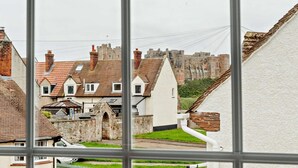 Une vue à travers une fenêtre donnant sur un quartier résidentiel, avec des maisons, un mur de pierre et un château en arrière-plan.