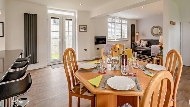 Un coin repas avec une table en bois dressée pour quatre personnes, un canapé et un téléviseur en arrière-plan.