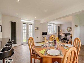 A dining area with a wooden table set for four, a sofa, and a TV in the background. - 2 Bed in Bamburgh (oc-92132) (Bamburgh)
