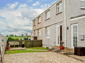 A two-story residential building with a gravel driveway, a wooden fence, and a small garden area with potted plants. - 2 Bed in Bamburgh (oc-92132) (Bamburgh)
