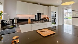 Une cuisine moderne dotée d’un îlot central, d’appareils électroménagers en acier inoxydable et de luminaires suspendus.