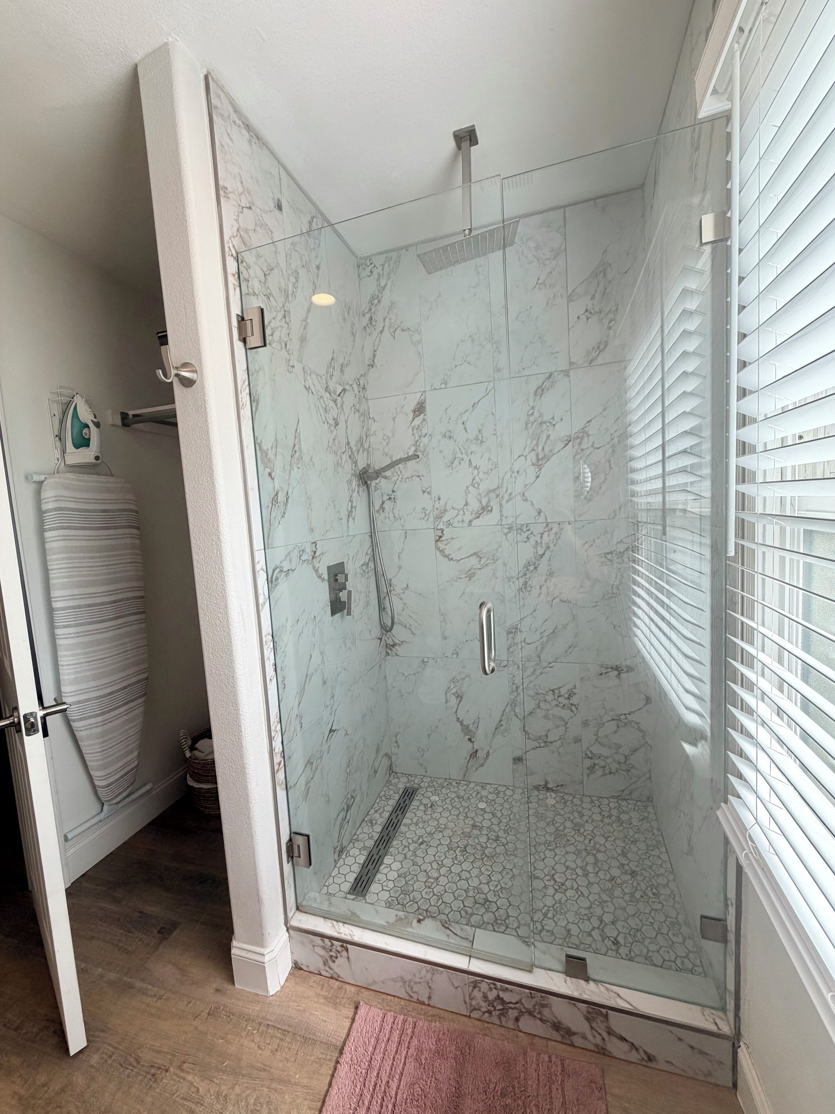 A glass-enclosed shower with marble tiles, a handrail, and a showerhead.