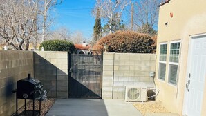 A patio with outdoor furniture, a grill, and a view of a gate and trees.