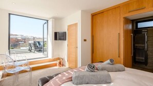 Et moderne soveværelse med en stor seng, en balkon med en stol og et fjernsyn monteret på væggen.