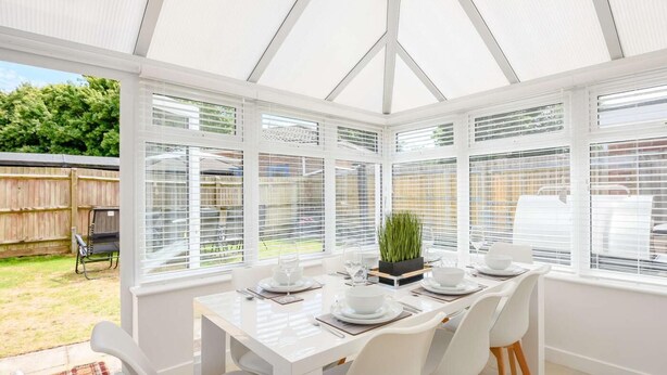 A conservatory with a white table set for four, surrounded by white chairs, and a small plant on the table. - 4 Bed in Christchurch (oc-87836) (Christchurch)