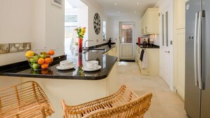 A modern kitchen with a central island, a dining area with wicker chairs, and a view of the city through large windows. - 4 Bed in Christchurch (oc-87836) (Christchurch)