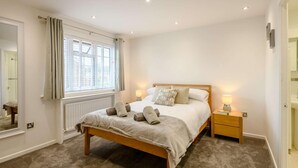A bedroom with a wooden bed, two bedside tables, a window with curtains, a radiator, and a mirror. - 4 Bed in Christchurch (oc-87836) (Christchurch)