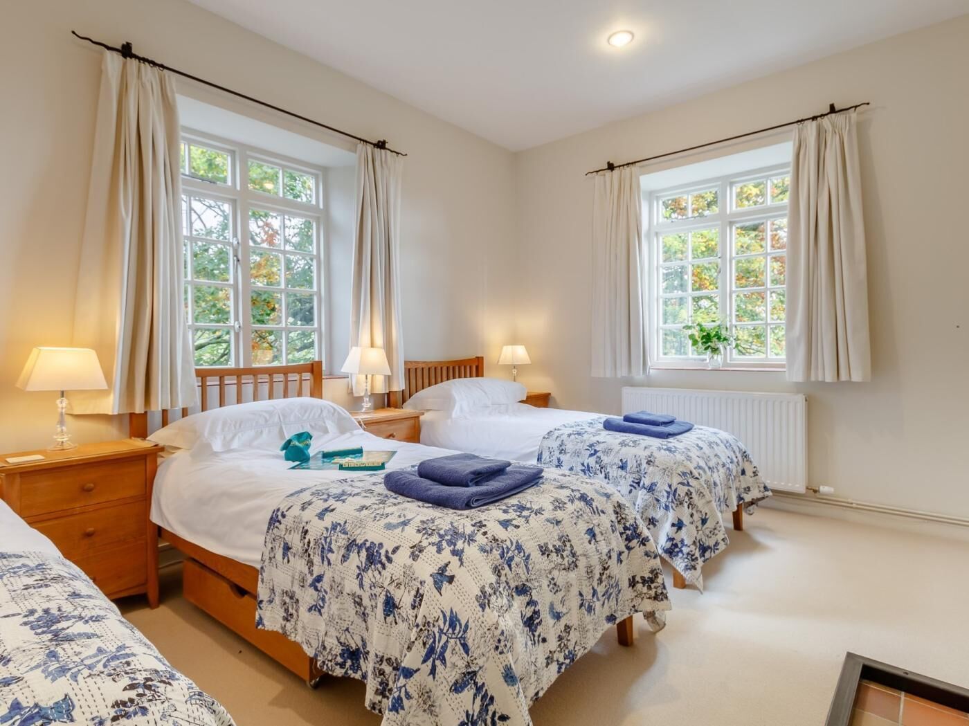 A hotel room with two beds, a window, a radiator, and a lamp on the nightstand.