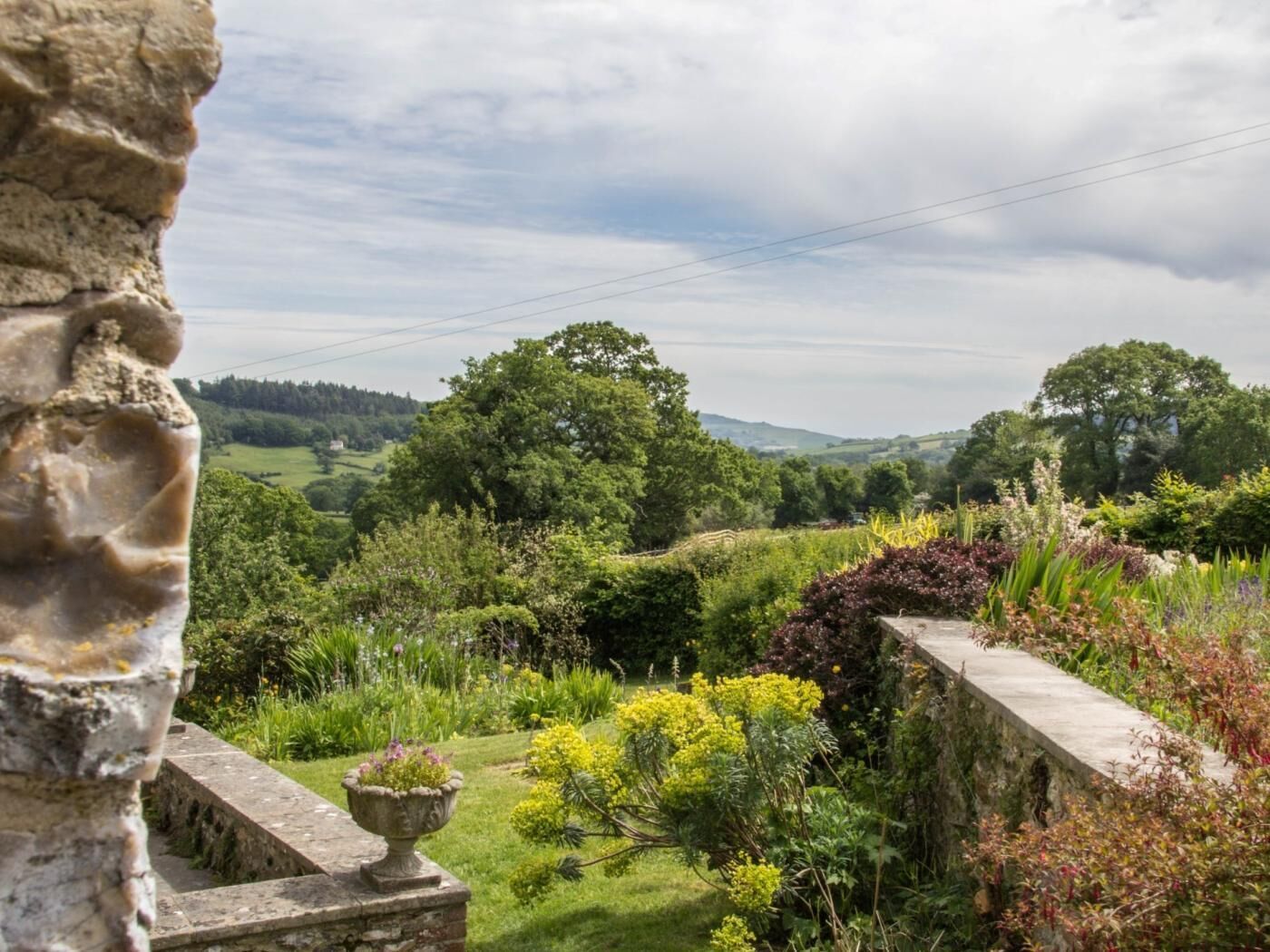 A stone structure with a garden view, including a variety of plants and a distant landscape.