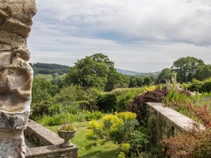 Eine Steinstruktur mit Blick auf einen Garten, der verschiedene Pflanzen und eine ferne Landschaft zeigt.