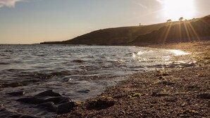 Un paysage côtier avec une plage, des vagues et une colline lointaine surmontée d’une construction.