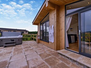 Une façade en bois, de grandes portes-fenêtres coulissantes, un jacuzzi et une terrasse en pierre.